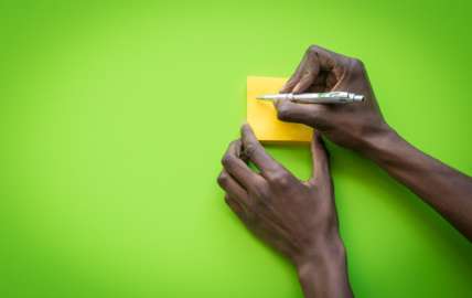 An image showing a hand writing on a yellow notepad, against a lime green background