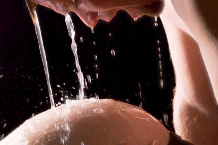 Image of a man, his head over the pregnant belly of a woman, whilst water pours from above.