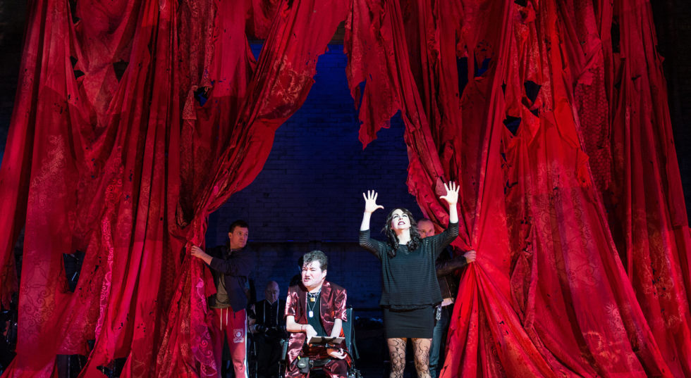 Three performers emerge from a red tattered curtain.