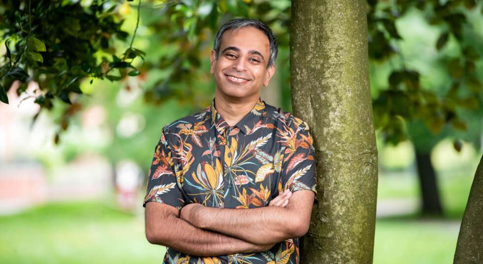 A photo showing Shahid Iqbal Khan, leaning against a tree in a park. He smiles broadly.